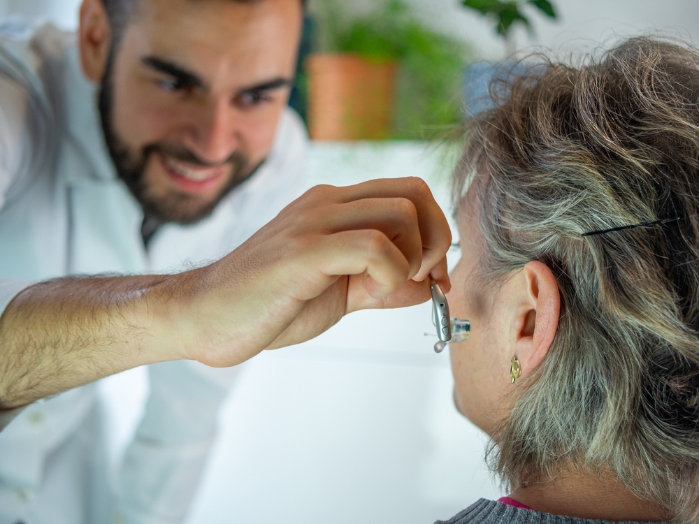 Young,Audiologist,Helping,To,Insert,An,Electronic,Hearing,Aid,To